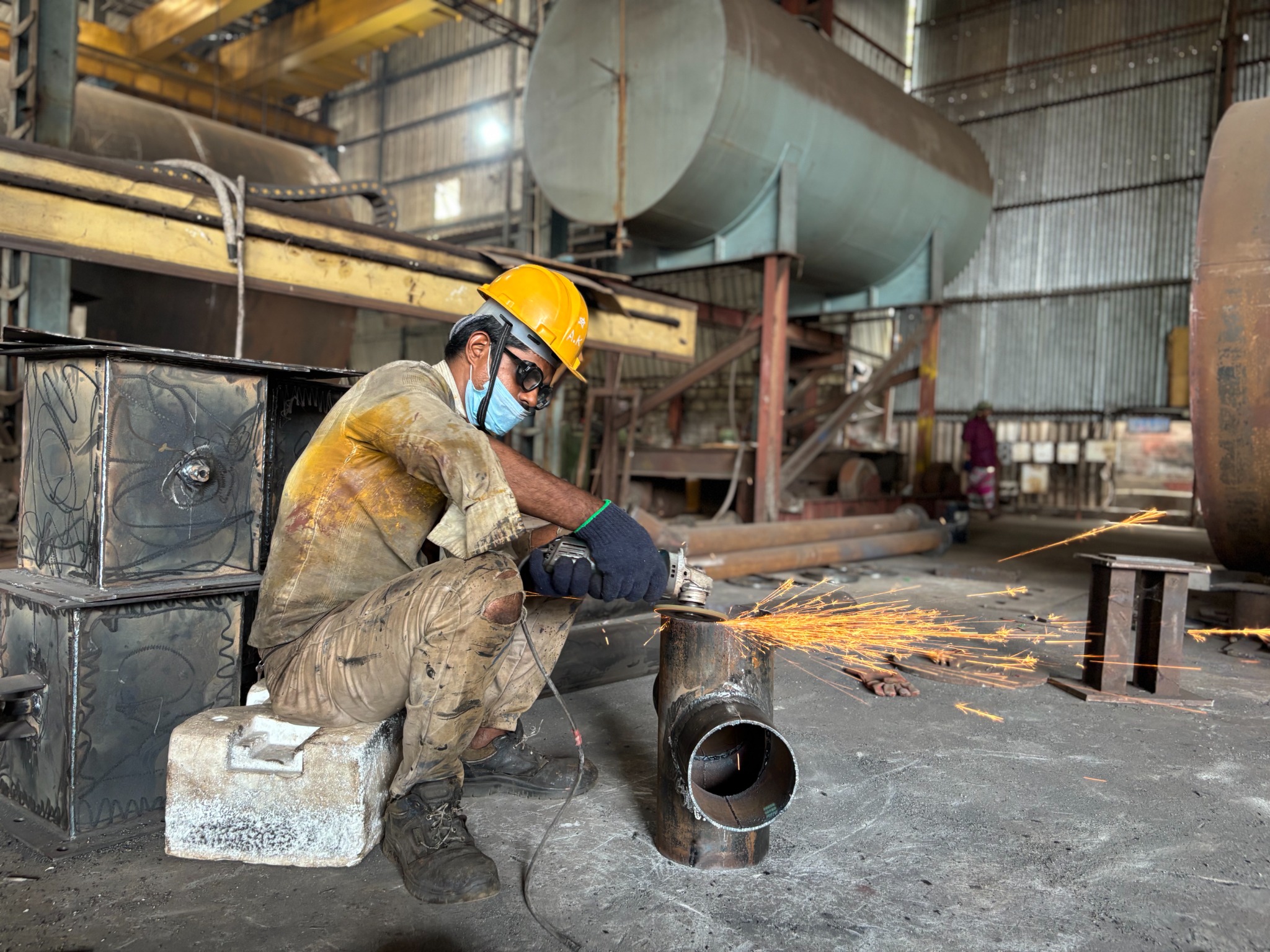 Worker grinding metal component in fabrication unit